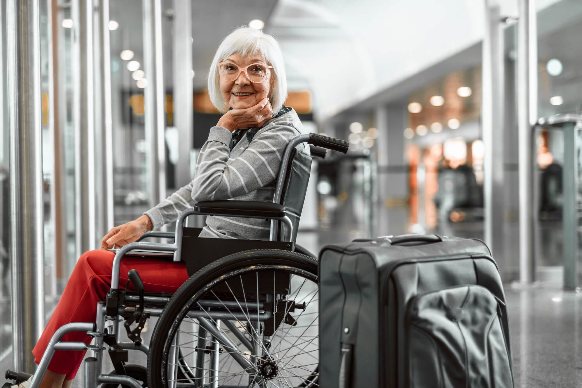Senior woman in a wheelchair with a suitcase at an airport.